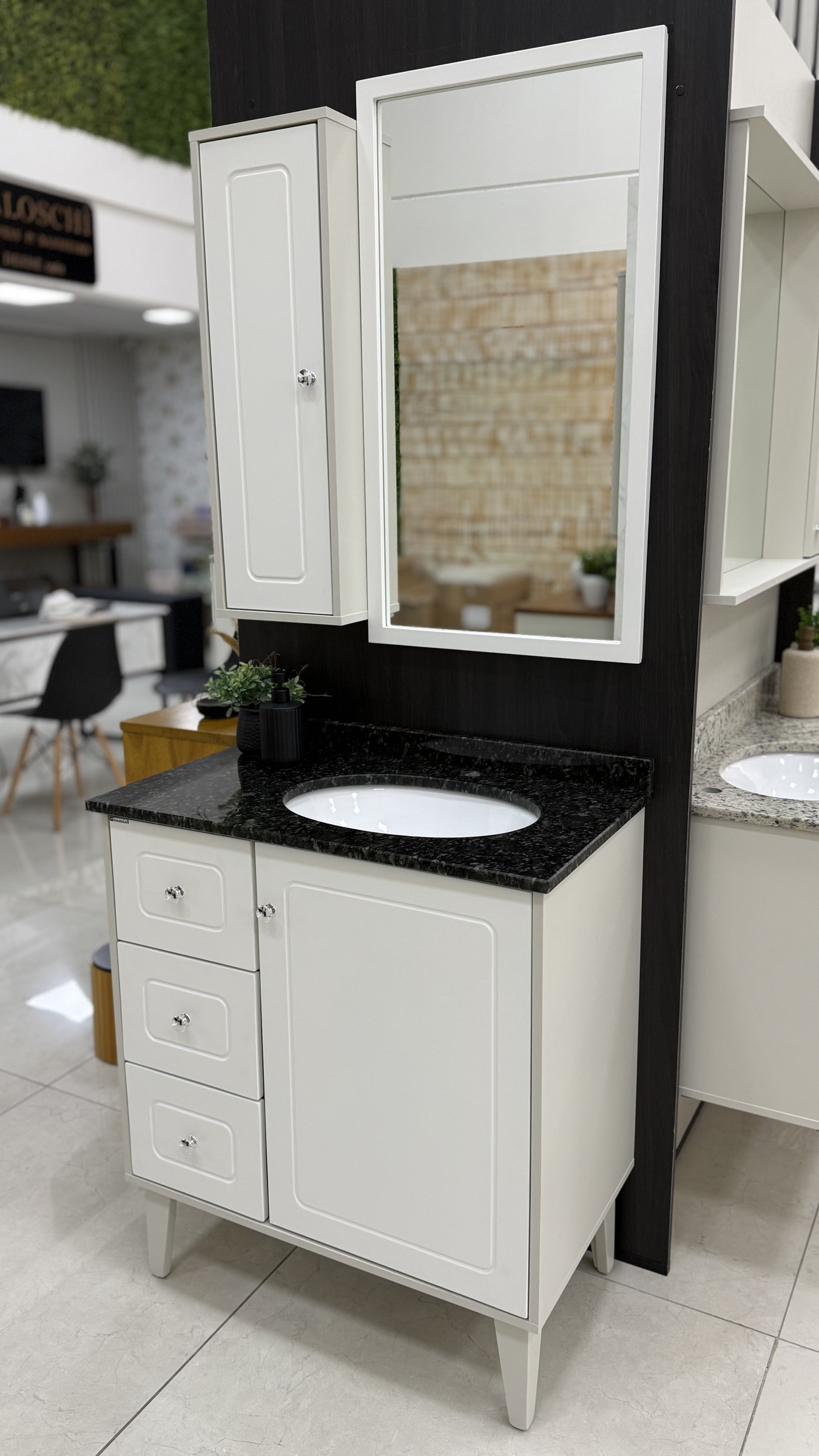 Fotografia real do Amalfi 80 cm branco com uma porta e três gavetas usinadas, pés, tampo de granito escuro, cuba branca embutida, espelho e armário lateral na loja