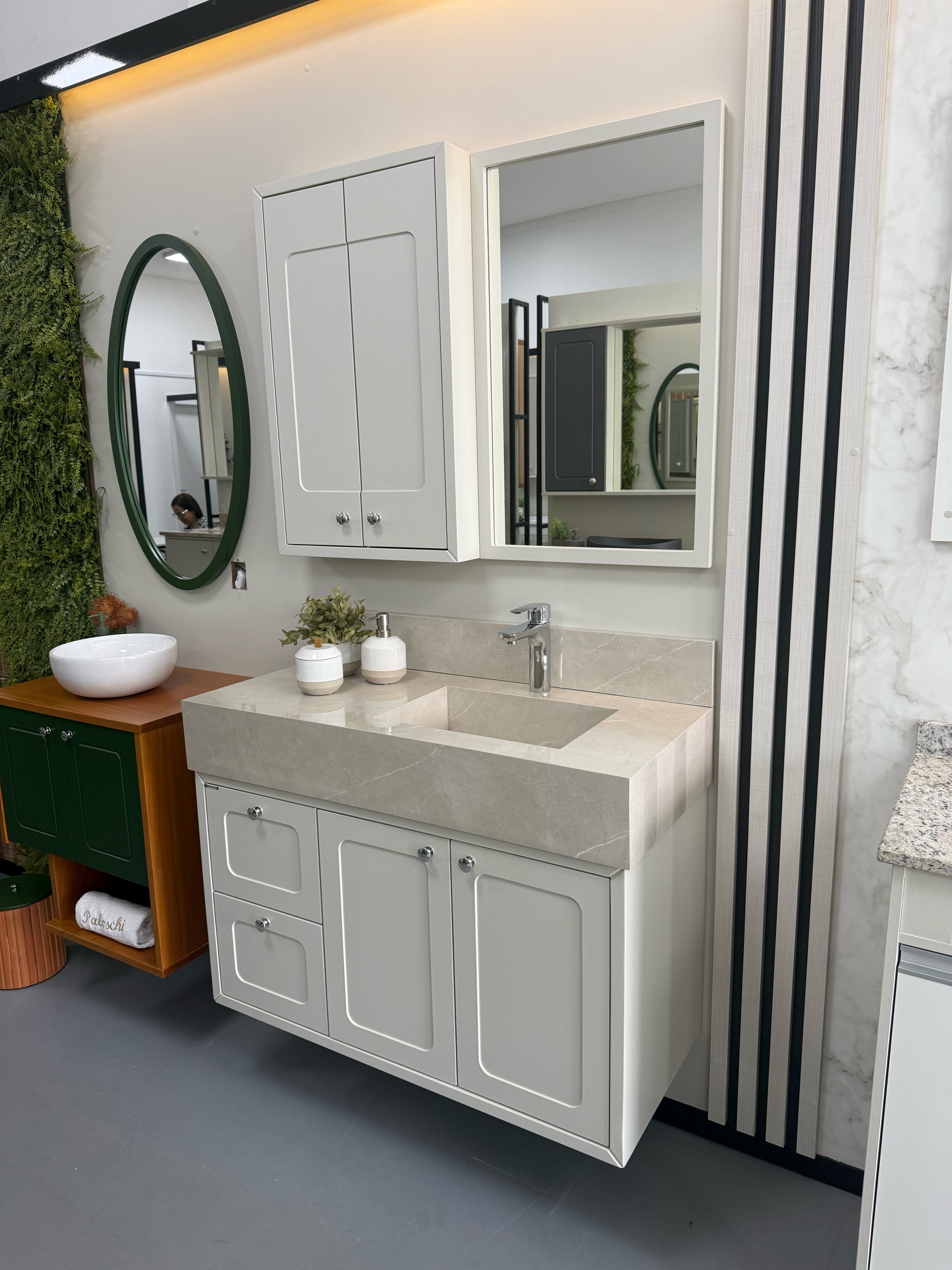 Foto real do conjunto Donatello branco 1,00 m com pia esculpida em porcelanato, balcão suspenso e espelheira na loja; móvel verde ao lado não incluso