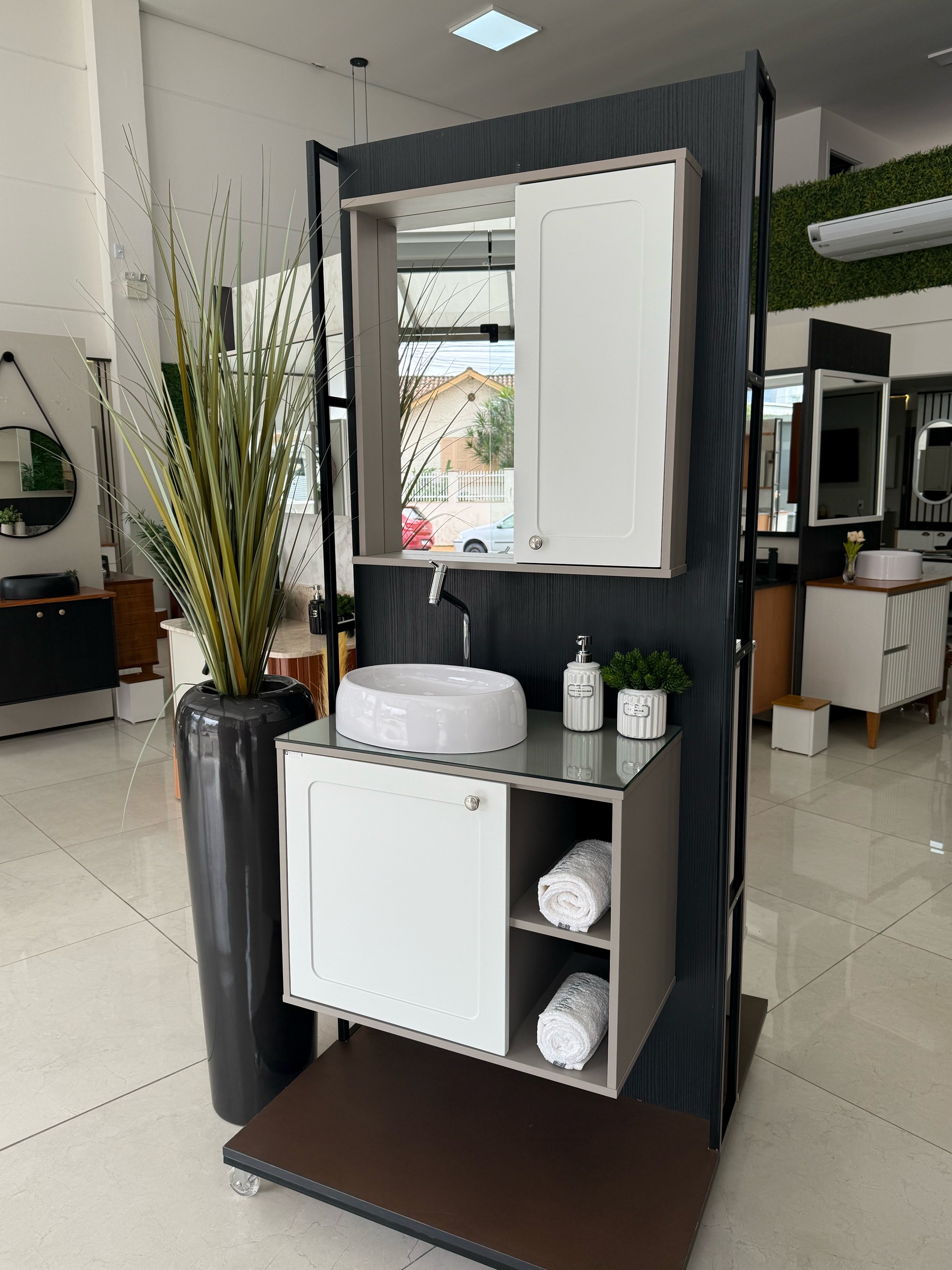 Fotografia real do Gissi Provenzale 68 cm suspenso, estrutura em tom taupe, portas claras em laca, dois nichos laterais, tampo de vidro, cuba branca de apoio e espelheira com porta lateral; base com rodízios apenas de exposição